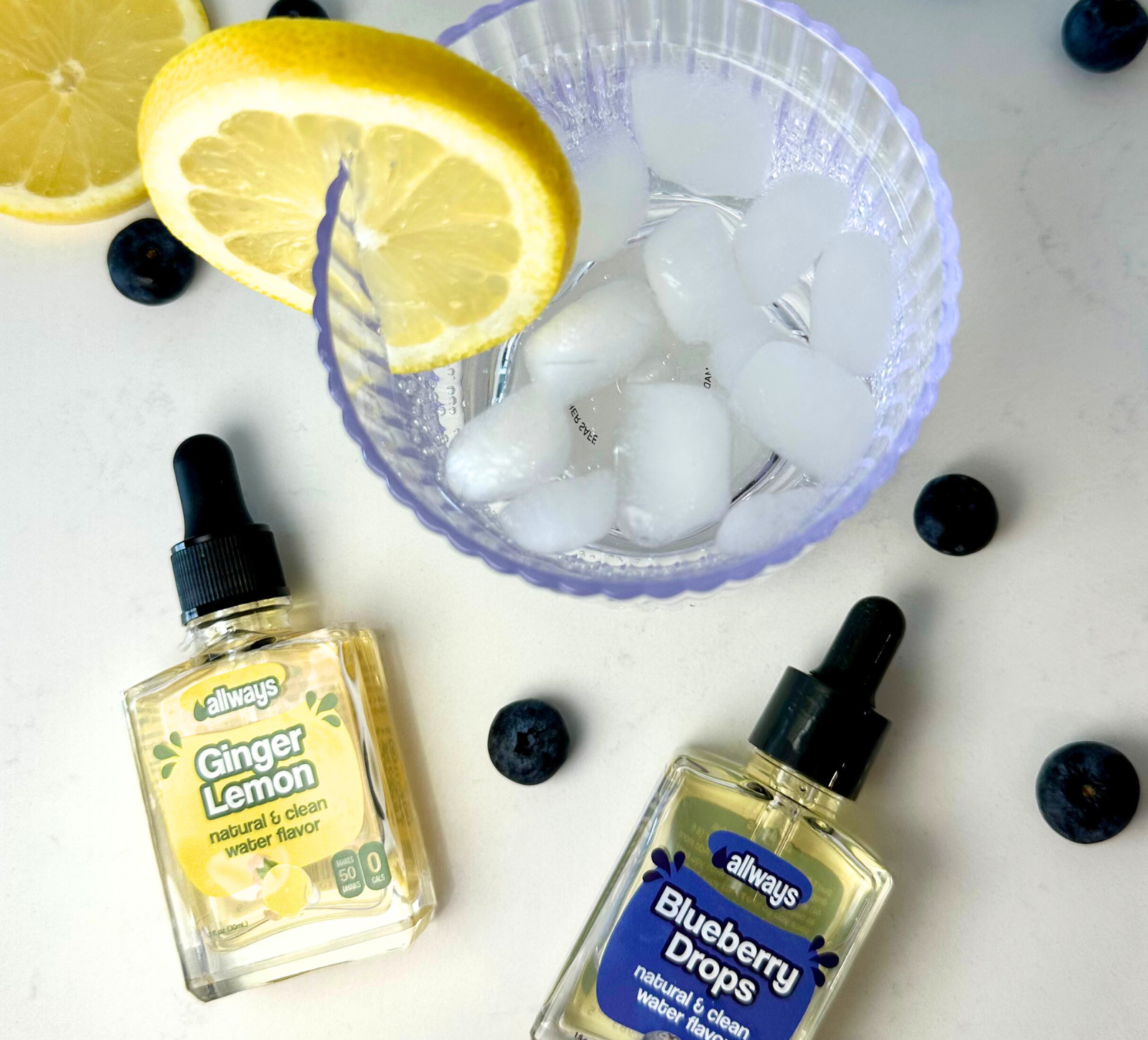 Allways Ginger Lemon Drops and Blueberry Drops laying next to a refreshing ice water drink with fresh lemon and blueberries