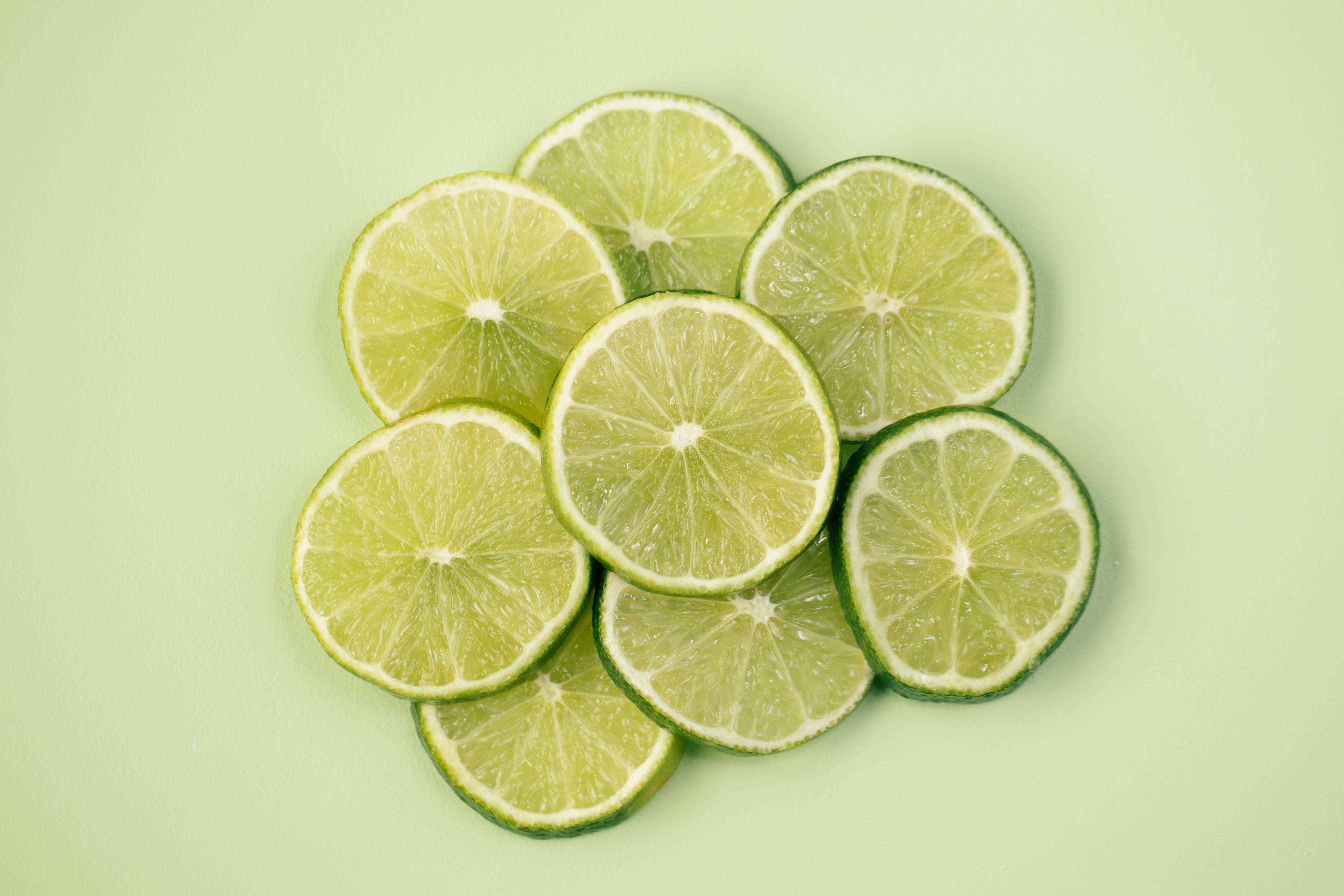 Fresh lime slices on a vibrant green background, highlighting the refreshing citrus flavor of Allways Drops