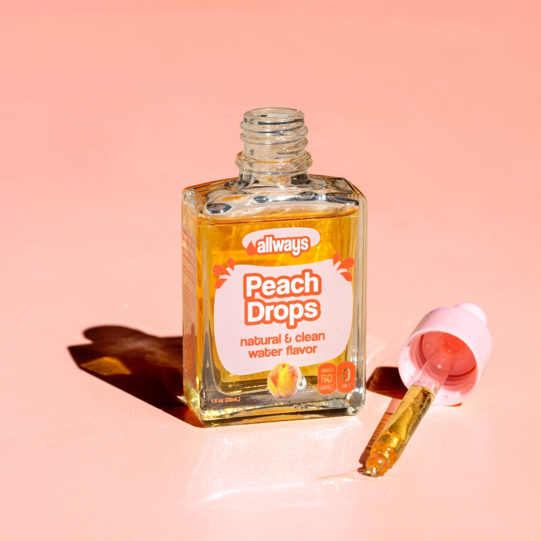 Allways Peach Drops with dropper laying next to glass bottle of peach drops in front of a peach colored background