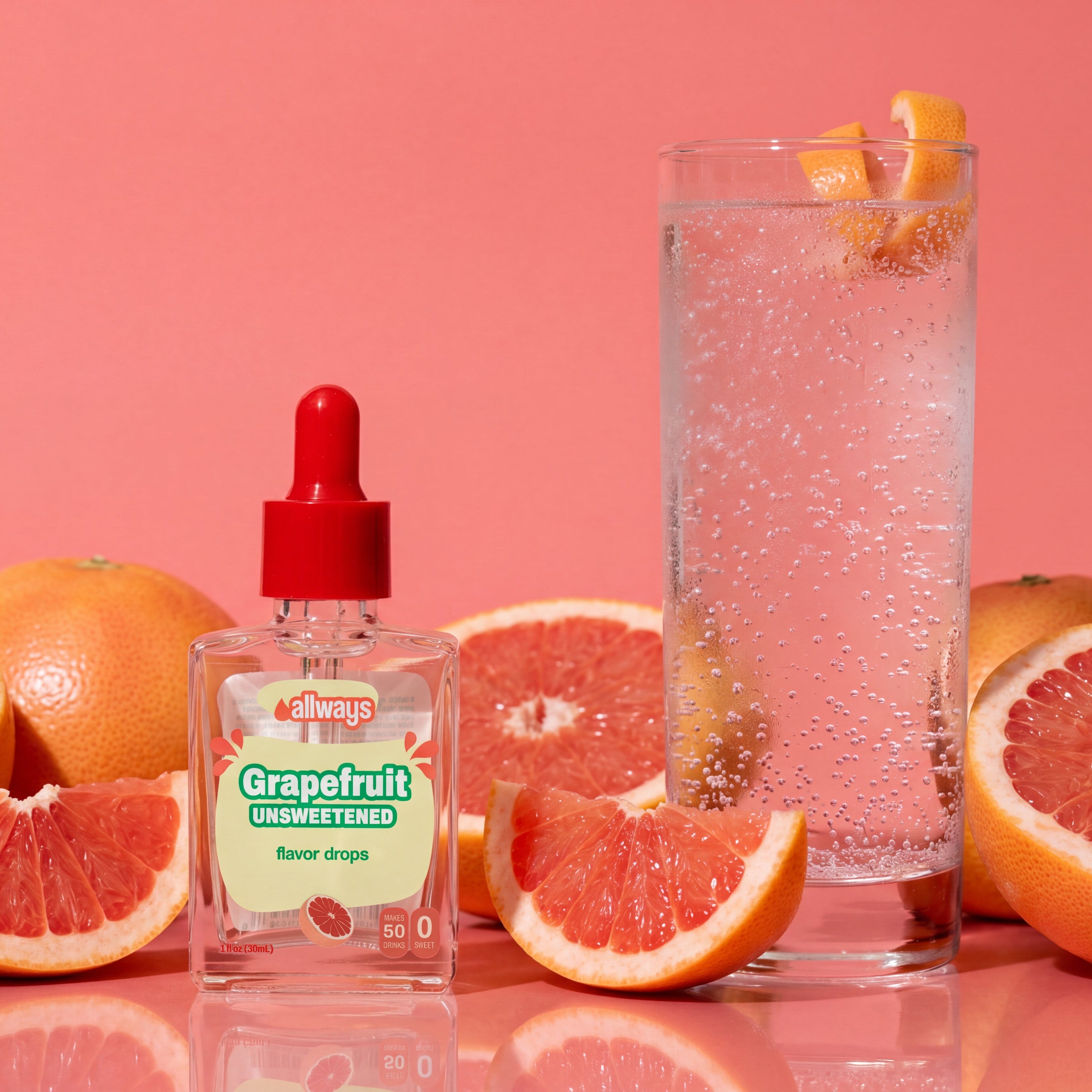 A bottle of Grapefruit Flavor Drops by Flavor Factory sits on a pink reflective surface, surrounded by grapefruit slices and whole grapefruits, next to a tall glass of bubbly pink beverage with grapefruit peel garnish, all against a solid pink background.