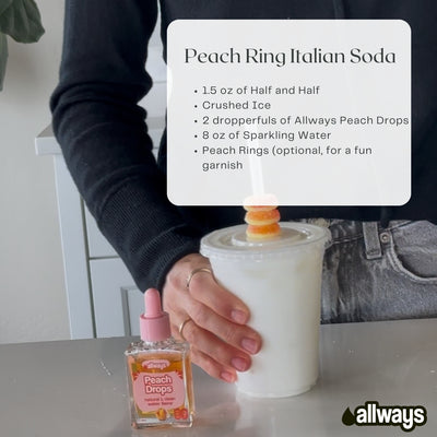 Person holding a Peach Ring Italian Soda with a recipe card and Allways Peach Drops bottle on a table.